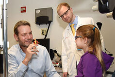 A pediatric physician works with a child patient in an exam room.